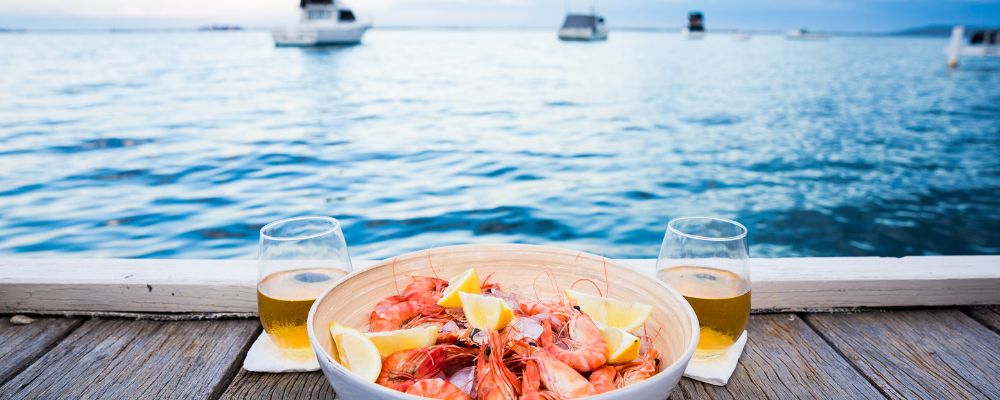 Bowl of shrimp and wine on a dock over the ocean