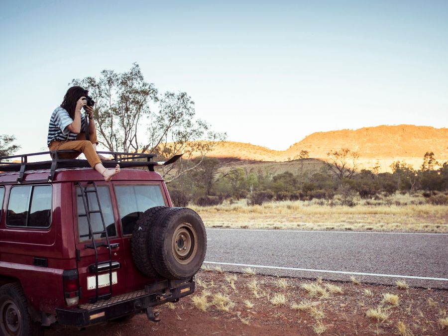 Woman photographing while sitting on car roof at desert by Alice Springs, Australia