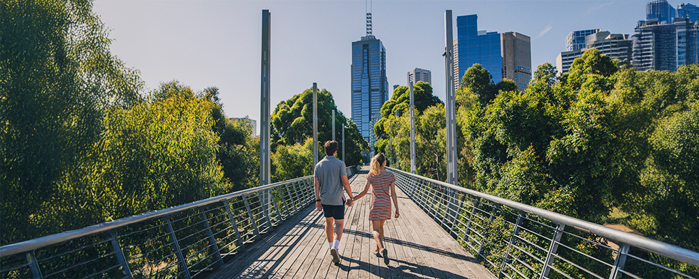 Couple walking on suspended bridge with city ahead