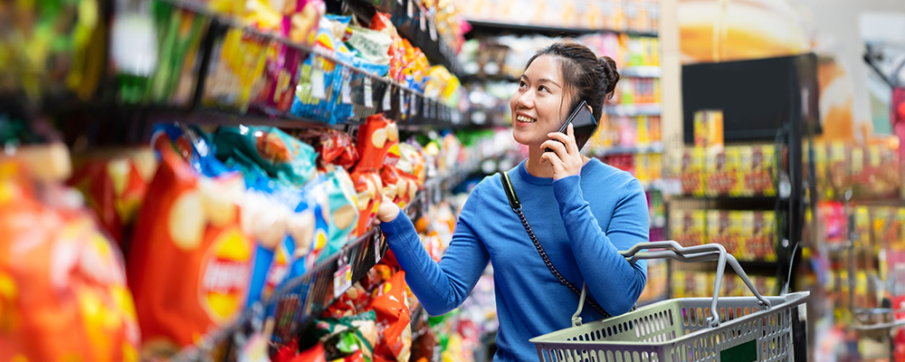 Woman talking on the phone carrying shopping basket inside supermarket